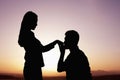 Silhouette of boyfriend kneeling and kissing his girlfriends hand at sunset