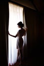 Silhouette of bride girl in the morning in full growth near window in dressing gown on wedding day Royalty Free Stock Photo
