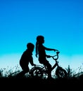 Silhouette of a brother and sister, cycling at sunset