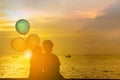 Silhouette of brother and sister sitting on the beach watching sunset with balloon in hand