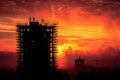 Silhouette of a building under construction covered in scaffolding and with workers in its highest part, with an intense red Royalty Free Stock Photo