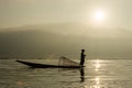 Silhouette Burmese fisherman wearing a hat standing at the back of a boat rowing with legs in the morning