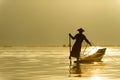 Silhouette Burmese fisherman wearing a hat standing at the back of a boat rowing with legs in the morning