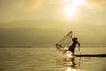 Silhouette Burmese fisherman wearing a hat standing on the back of a boat using fishing equipment Royalty Free Stock Photo