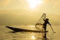 Silhouette Burmese fisherman wearing a hat standing on the back of a boat using fishing equipment in the morning The mist faded at Royalty Free Stock Photo