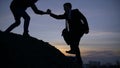 Businessman silhouette gived hand for pull team to peak mountain work together