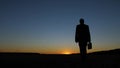 Silhouette of businessman with briefcase walking across field at sunset, against a blue sky Royalty Free Stock Photo