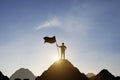 Silhouette of businessman holding flag on the top of mountain with over blue sky and sunlight. It is symbol of leadership