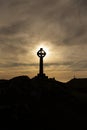 Silhouette of a Celtic cross with the evening sun directly behind it. With a cross in the background