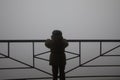 Silhouette of a child holding handrail and looking towards fog mist