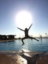 Silhouette of a child jumping in a swimming pool with open arms and legs with the round large light of th sun just above her Royalty Free Stock Photo