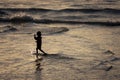 A silhouette of a child playing on a beach at sunset with reflections on the wet sand and waves behind Royalty Free Stock Photo
