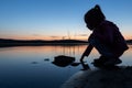 Silhouette of a child touching the lake water at sunset, blue hour. Calmness and silence on the lake. Royalty Free Stock Photo