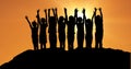 Silhouette children with hands raised on hill against orange sky