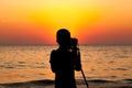 Silhouette of the children using dslr camera and tripod take photo of sunset on the beach., with beautiful light of sunset