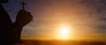 Silhouette of christian holding cross in hands to praying for blessing from god at sunset