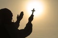 Silhouette of christian Man holding a cross cross in hands praying for blessing from god on sunlight background, hope concept Royalty Free Stock Photo