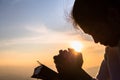 Silhouette of christian young woman praying with a cross and open the bible at sunrise, Christian Religion concept background