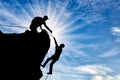 Silhouette of a climber who helps to climb the top of a man, throws him a rope and holds out his hand