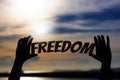 Silhouette, Close up Hand holding FREEDOM text with blurred sea sunset