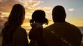 Silhouette closeup of happy family with one child on the beach looking at view at sunset. Two parents and daughter Royalty Free Stock Photo