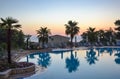 Silhouette coconut palm tree with umbrella and chair at sunrise time around outdoor swimming pool Royalty Free Stock Photo