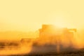 Silhouette of combine harvester in clouds of dust on the field at sunset.