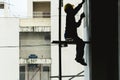 Silhouette of a construction worker sitting on some scaffolding and applying putty to a wall of a building. Royalty Free Stock Photo