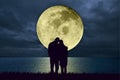 Silhouette of couple embracing standing at the beach at night watching the moonlight from a big full moon shining in the ocean. Lo