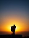 A silhouette of a couple man and woman with coats on watching the sunset from a cliff with the sky and ocean behind them on a Royalty Free Stock Photo