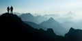 Silhouette Couple of man and woman reaching mountain top enjoying freedom and looking towards blue mountain silhouettes Royalty Free Stock Photo