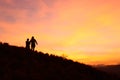 Silhouette of a couple of young female hikers watching the sunrise amidst a beautiful warm toned cloudscape at the top of a grassy Royalty Free Stock Photo