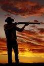 Silhouette of cowboy with shotgun aimed in sunset