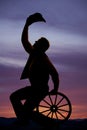 Silhouette cowboy sitting on wagon wheel hold hat up