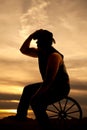 Silhouette cowboy sitting on wagon wheel touch hat Royalty Free Stock Photo