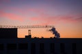 Silhouette of crane and buildings. Smoke from industrial chimney. Sunrise in the city Royalty Free Stock Photo