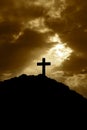 Silhouette of a cross on top of a mountain at sunset. With the suns rays shining down