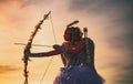 Silhouette of a cupid. Side view of teen girl archer against sunset. Little Cupid girl aiming at someone with an arrow Royalty Free Stock Photo