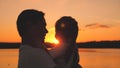 Silhouette of a dad hugs his little daughter at sunset in the sky and smiles. Happy Dad's Day. The girl sits in her Royalty Free Stock Photo