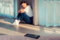 A silhouette of a depresed woman in a blur, sitting on the floor. In the foreground is a smartphone. Copy space. The concept of