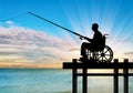 Silhouette of a disabled man in a wheelchair with a fishing rod in his hand fishing near the water on the pier Royalty Free Stock Photo