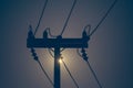 Silhouette of electricity pole and high voltage power line with sunset in the background.