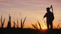 Silhouette of a farmer in a field. Looks forward, holds the scythe for mowing the grass behind his shoulder