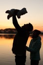 Silhouette of father holding little baby in his hands and mother behind on sunset with lake on background. Man with child. Family Royalty Free Stock Photo
