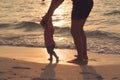 Silhouette of father and little daughter learning to walk at sunset beach. Female infant ten months old. Happy family Royalty Free Stock Photo