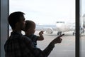 Silhouette Of Father And Son Looking And Pointing By Fingers At Airplane Through The Window Of Airport Terminal. Family Journey,