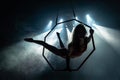 Silhouette of female Aerial acrobat on circus stage with spot lights on background