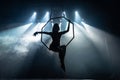 Silhouette of female Aerial acrobat on circus stage with spot lights on background