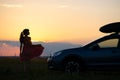 Silhouette of female driver standing near her car on grassy field enjoying view of bright sunset. Young woman relaxing during road Royalty Free Stock Photo