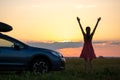 Silhouette of female driver standing near her car on grassy field enjoying view of bright sunset. Young woman relaxing during road Royalty Free Stock Photo